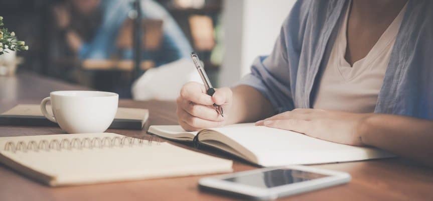 A person writing down ideas in a notebook and preparing to start a blog