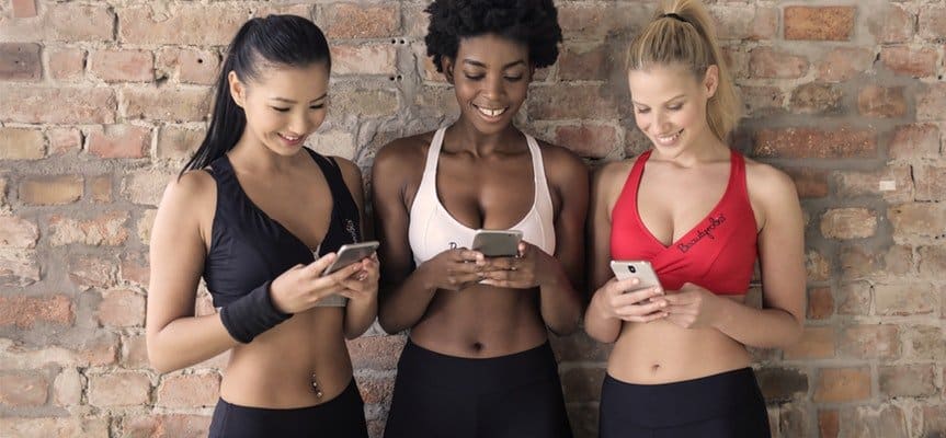 Three young women in sports apparel looking at their smartphones and excited with their first dropshipping sales. 